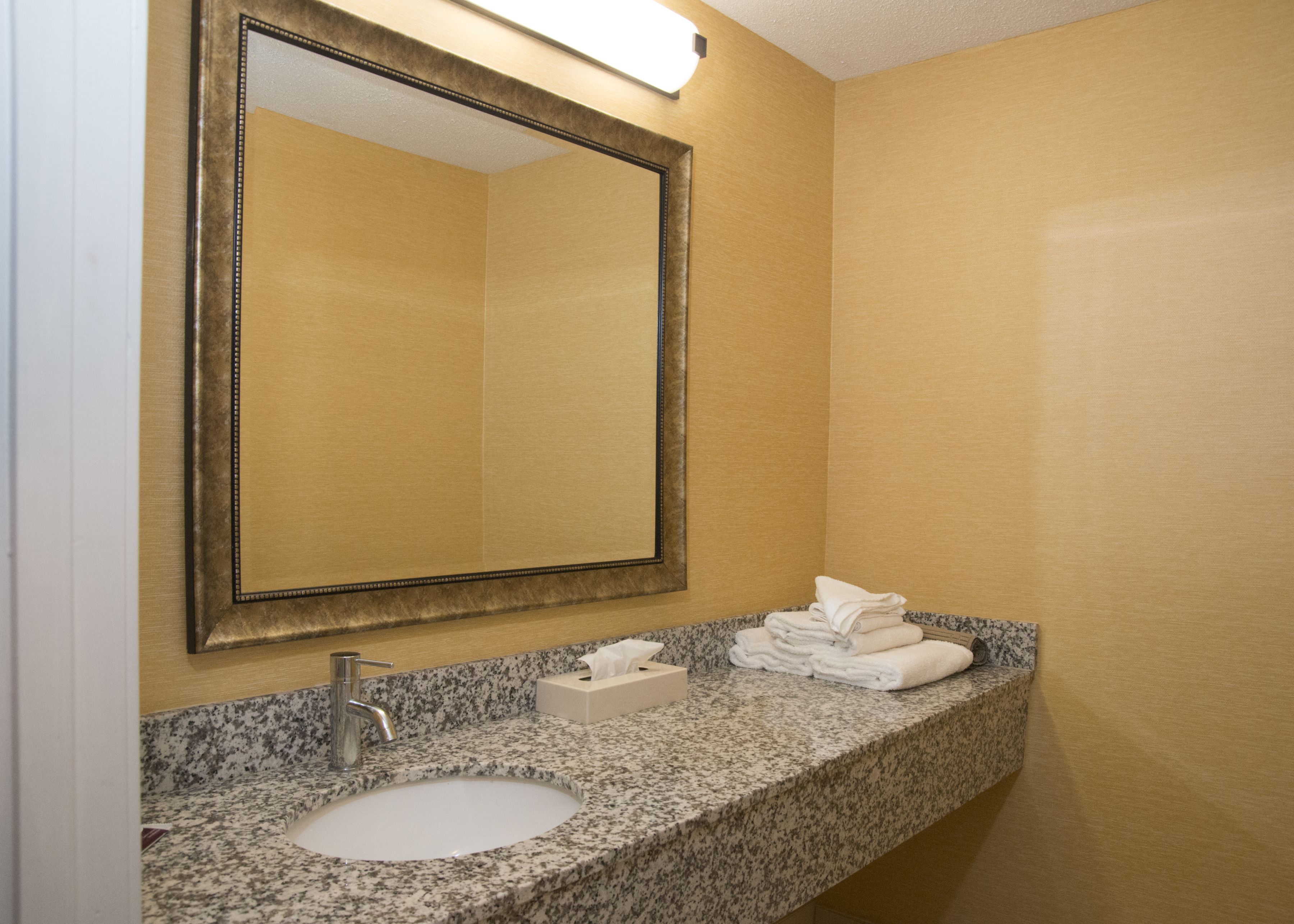 A bathroom with a granite countertop sink, a mirror, and a towel rack.