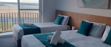 A hotel room with two beds, a large window with a view of the beach, and a painting on the wall.