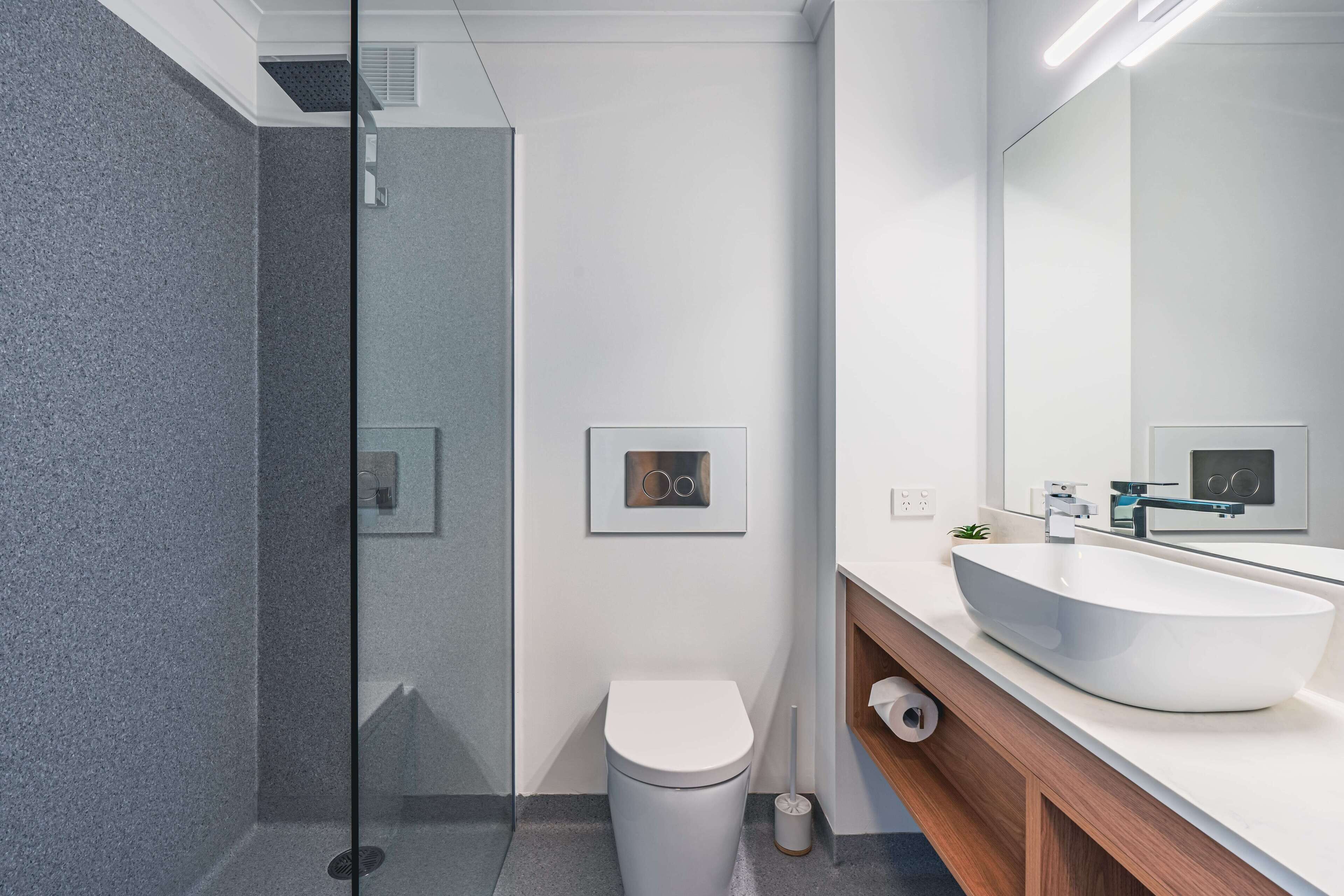 Ein modernes Badezimmer mit Duschkabine aus Glas, Toilette in Weiß, einem großzügigen Waschtisch und einem Spiegel darüber.