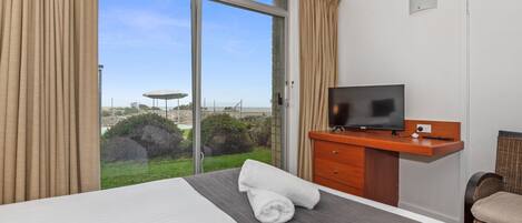 A hotel room with a bed, a TV on a wooden desk, and a view of the outdoors.