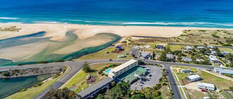 An aerial view of a coastal area with a large building, roads, and a beach.