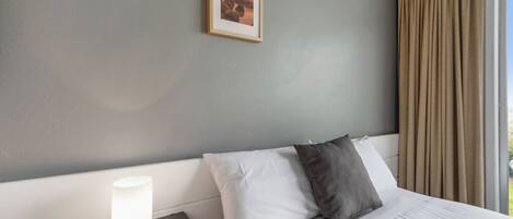 A hotel room with a bed, a bedside lamp, a framed picture on the wall, and a window with curtains.