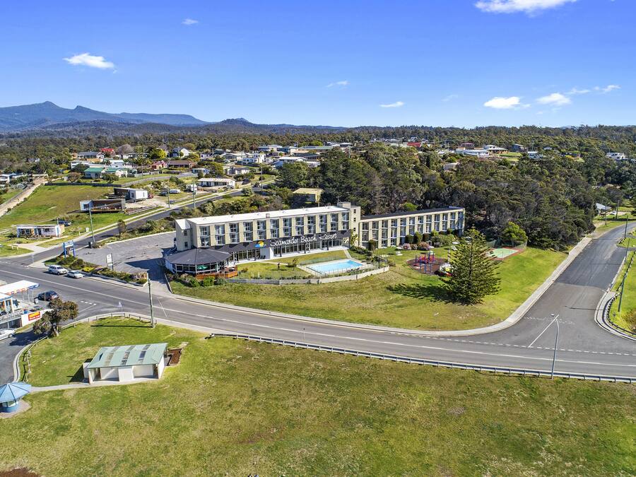 A modern building with a swimming pool, surrounded by green lawns and a road.