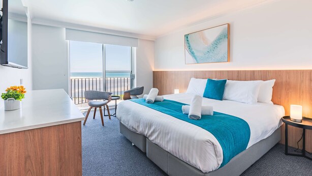 A hotel room with a bed, a desk, a chair, a bedside table, a TV, a window, and a balcony.
