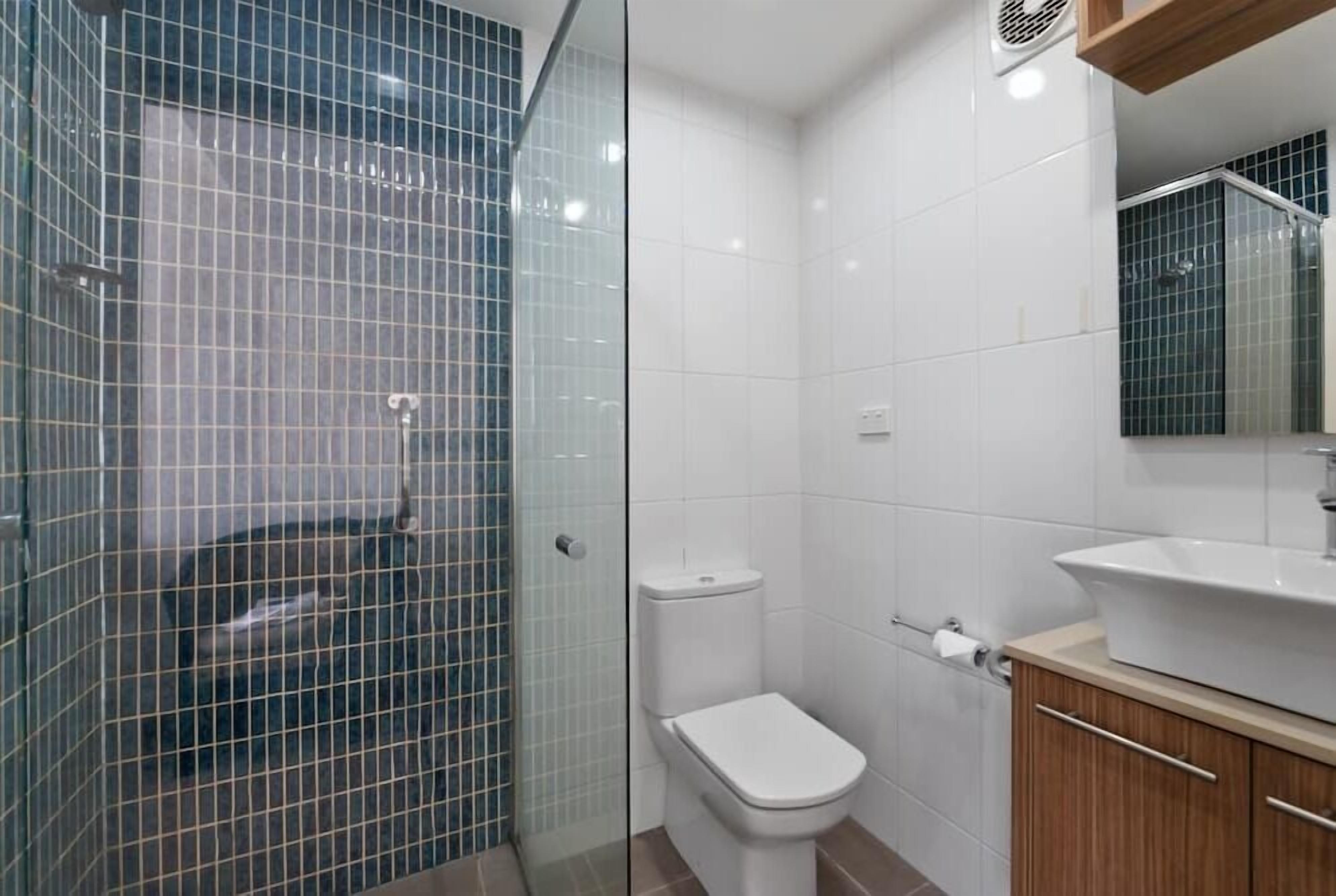 A bathroom with a glass-enclosed shower, a white toilet, and a sink with a mirror above it.