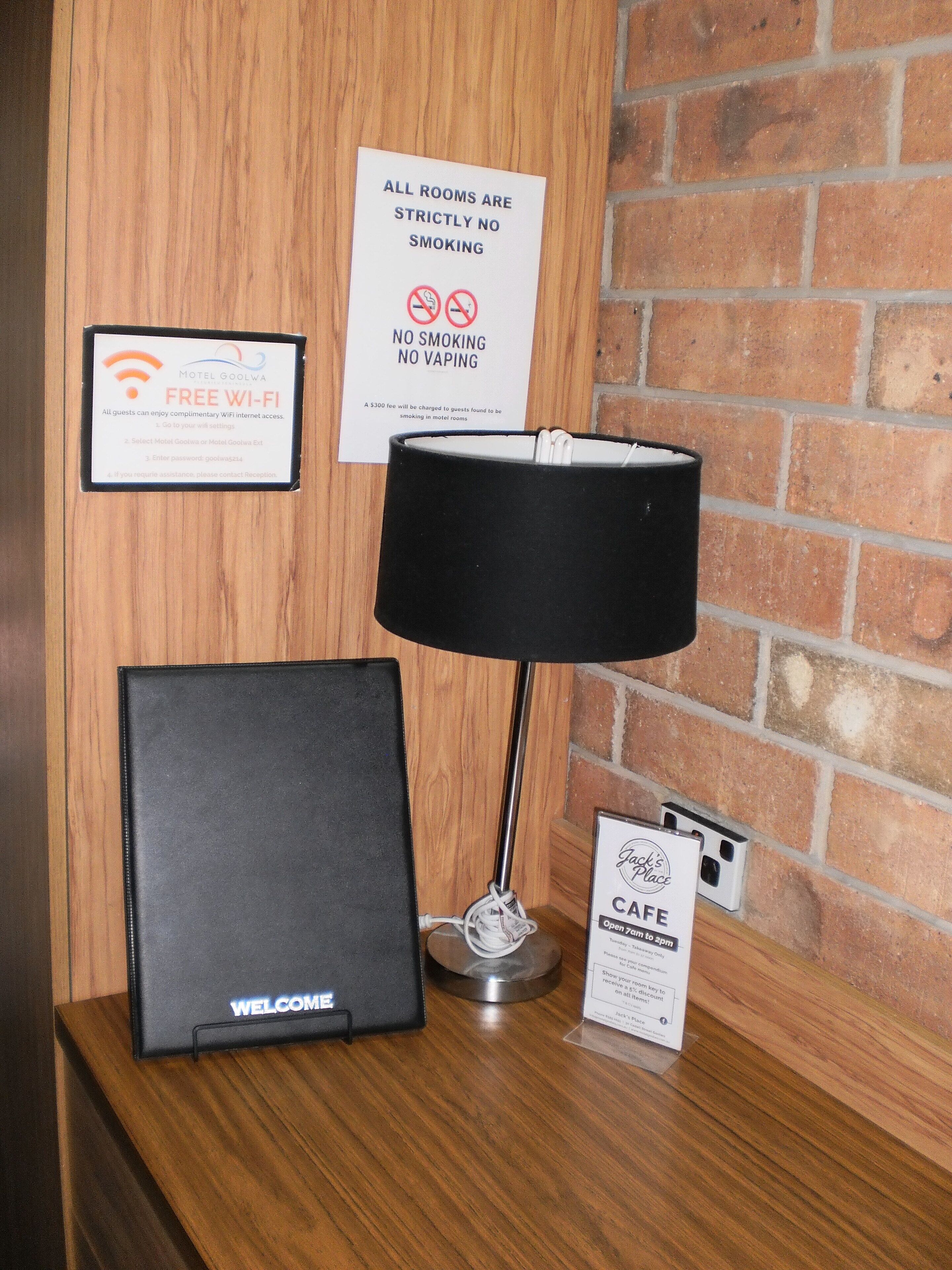 Una mesa de recepción con una lámpara negra, un cartel que indica Wi-Fi gratuito, un letrero de no fumar y un letrero de bienvenida.