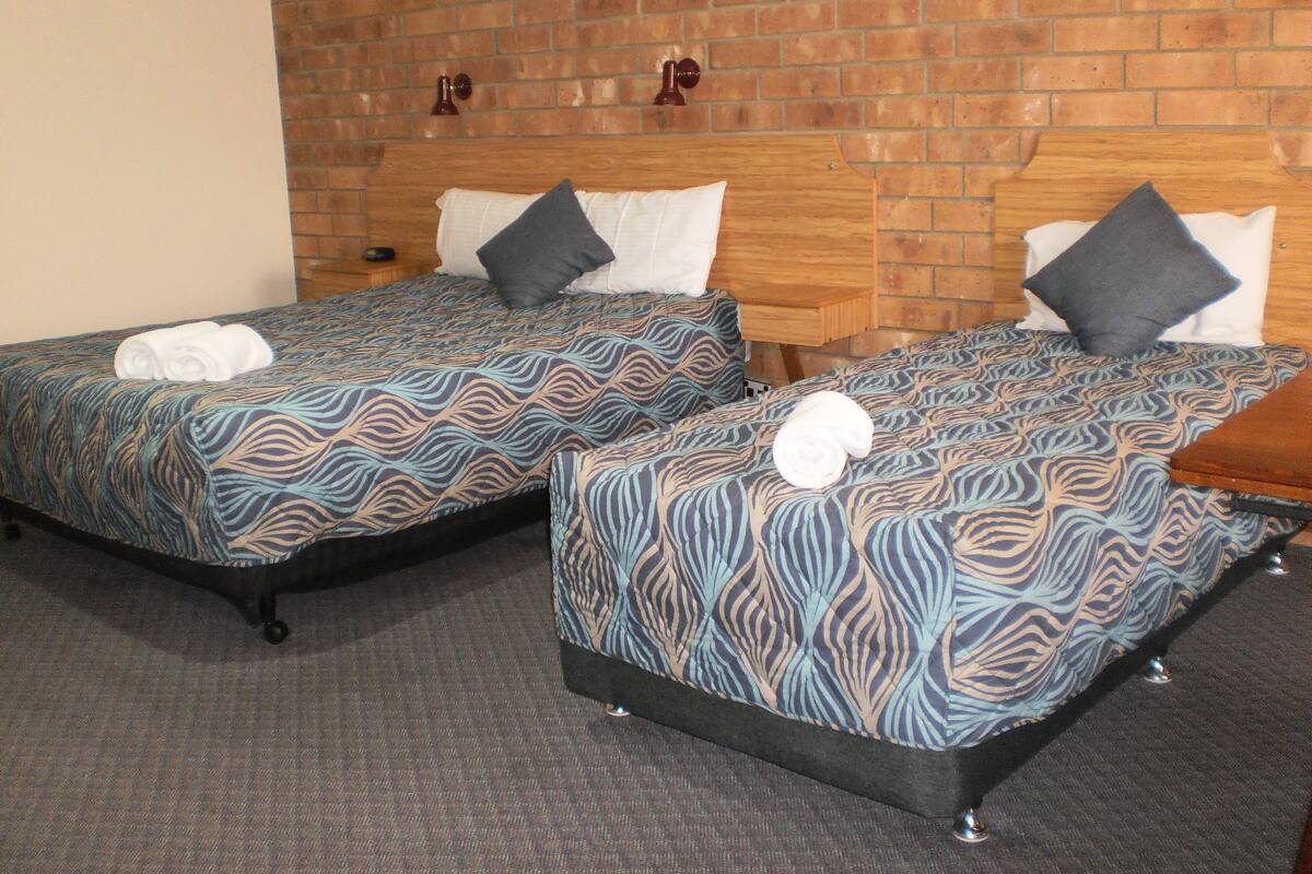 Two twin beds with patterned bedding, a brick wall, and a wooden headboard.