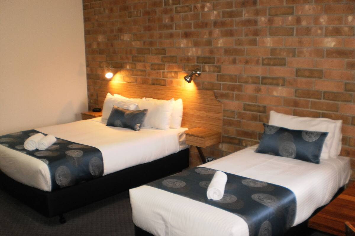 Two twin beds with matching headboards, a brick wall, and a nightstand with a lamp.