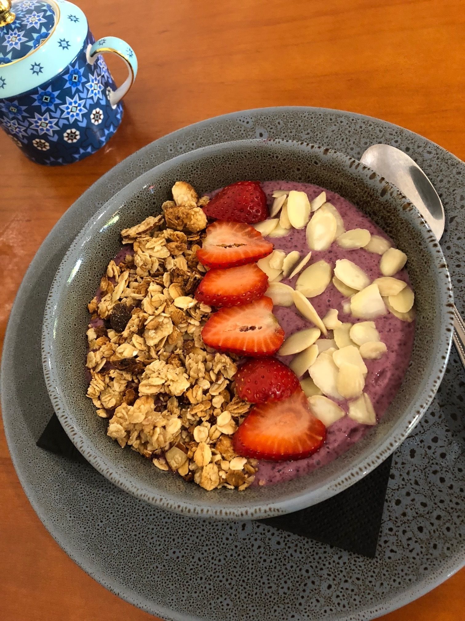 A bowl of oatmeal with strawberries and almonds on a speckled plate.