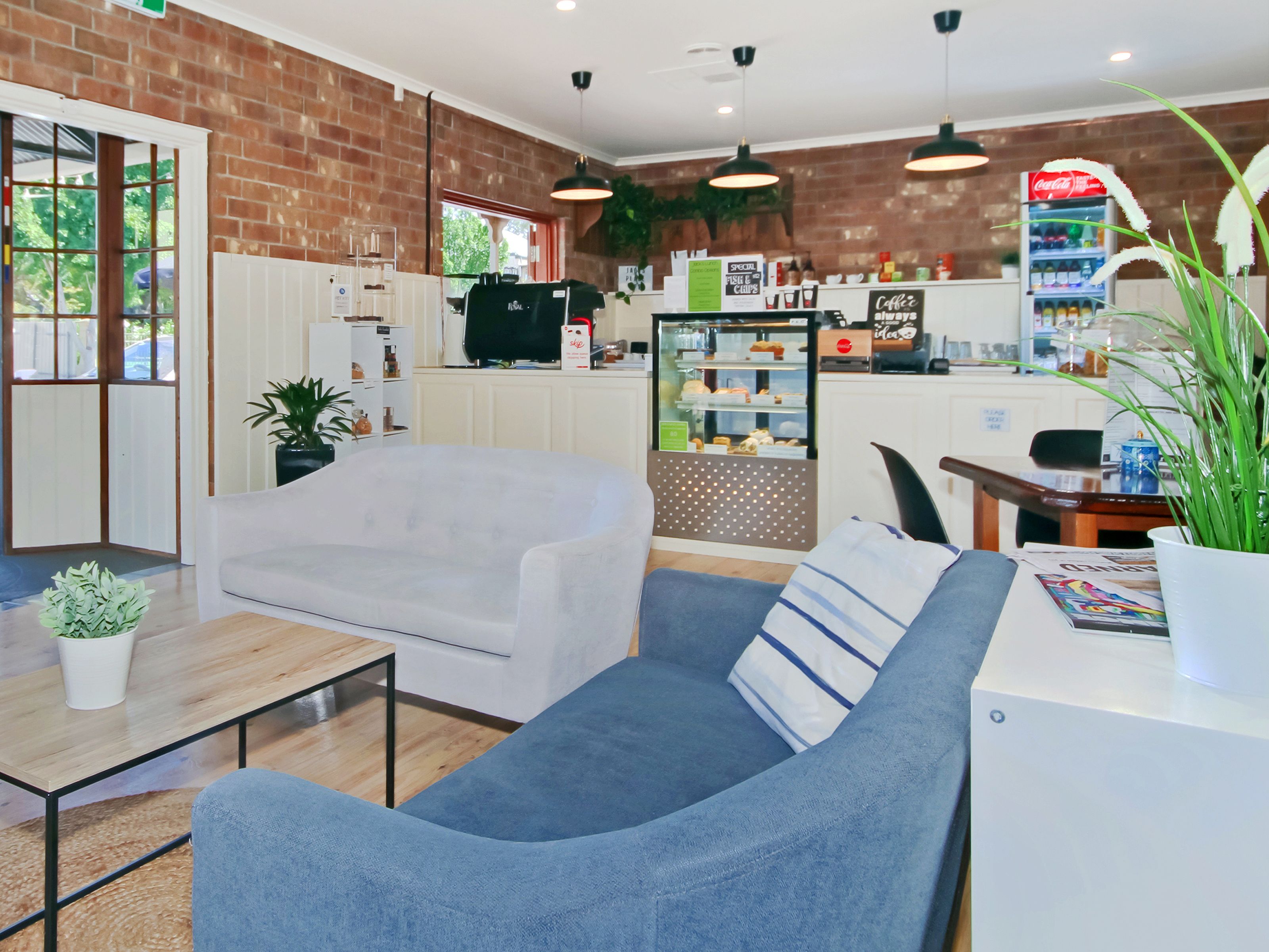 A modern interior with a brick wall, a white sofa, a dining table, and a kitchen area with a refrigerator and a Coca-Cola fridge.