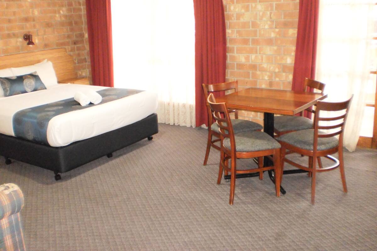 A hotel room with a bed, a dining table with chairs, and a brick wall.