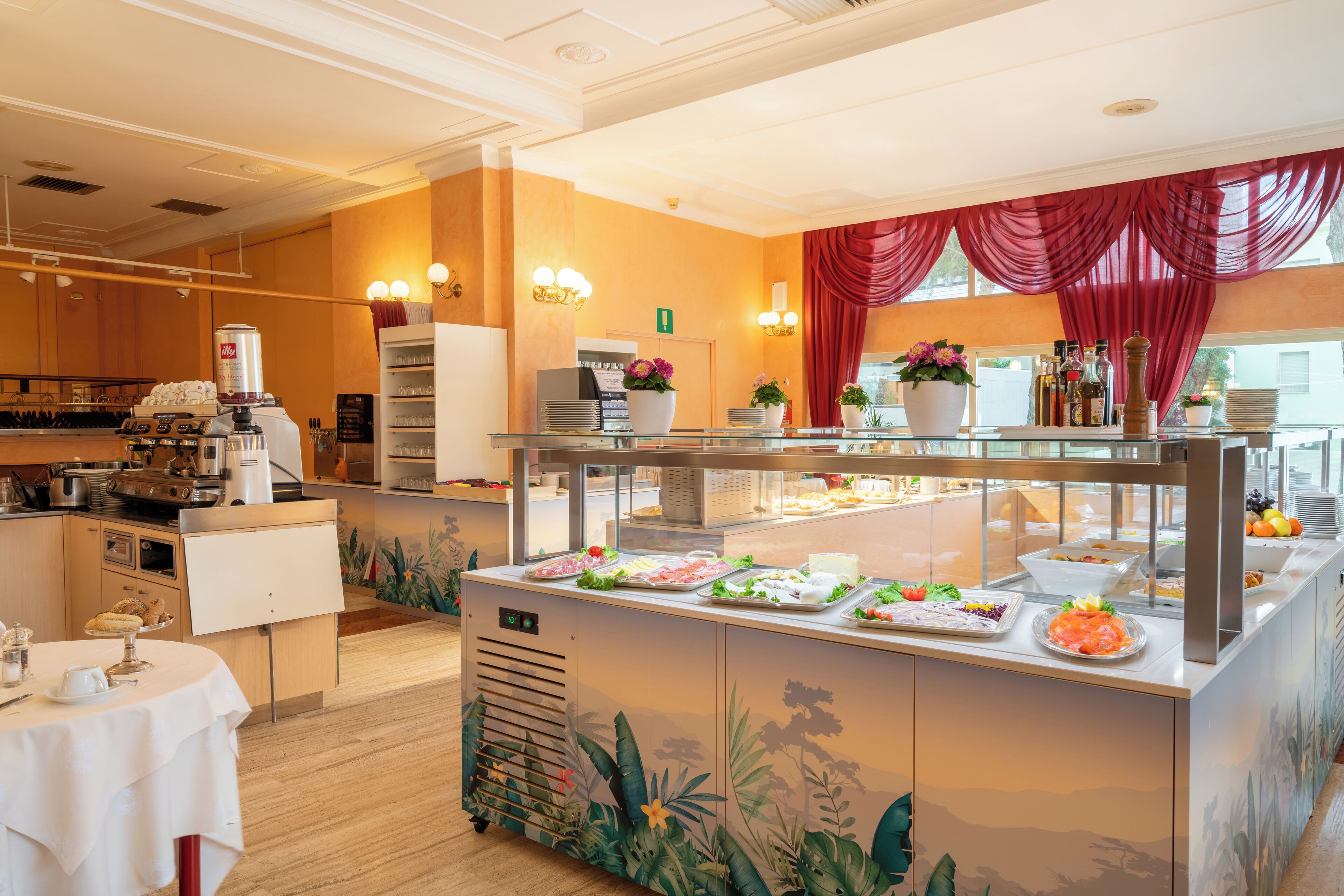 Zona de bufé con diversas opciones de comida, una estación de café y un área de estar con una mesa dispuesta para dos.