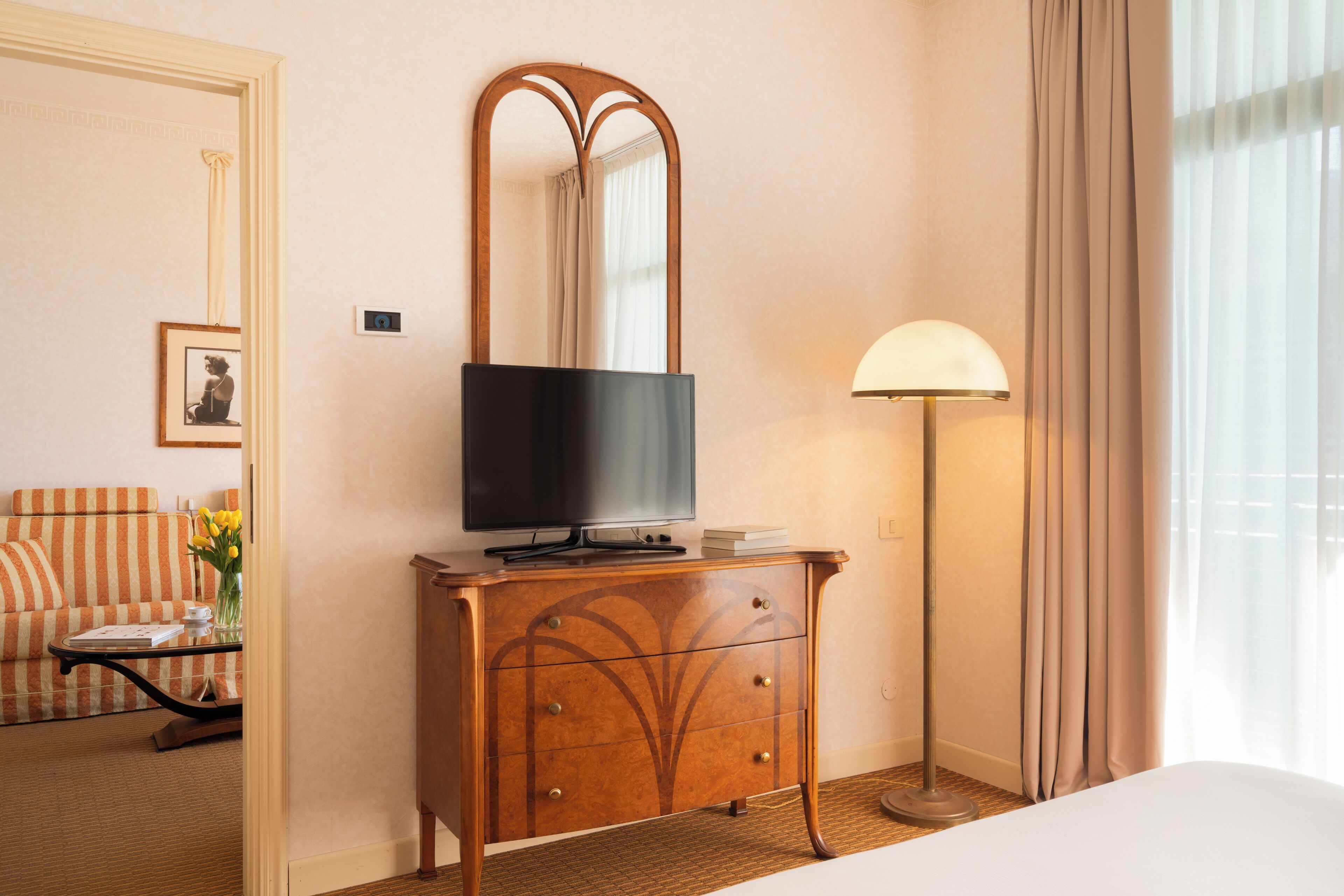 Une chambre d’hôtel avec une commode en bois, un téléviseur posé dessus, une lampe, un lit, un canapé et un miroir au mur.