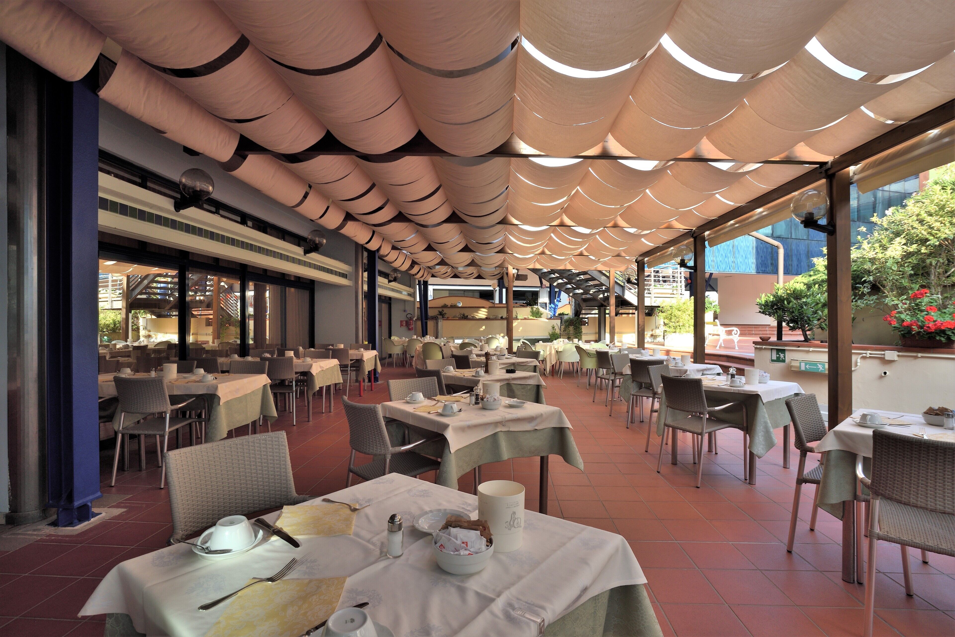 Un espacio de comedor al aire libre con mesas y sillas, cubierto por un toldo estampado.
