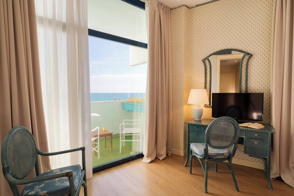Une chambre avec un balcon, un bureau avec une télévision et deux chaises.