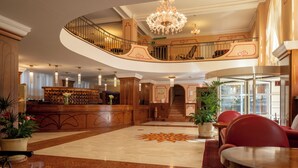 A grand lobby with a curved staircase, a reception desk, and a chandelier. - Grand Hotel Astoria (Grado)