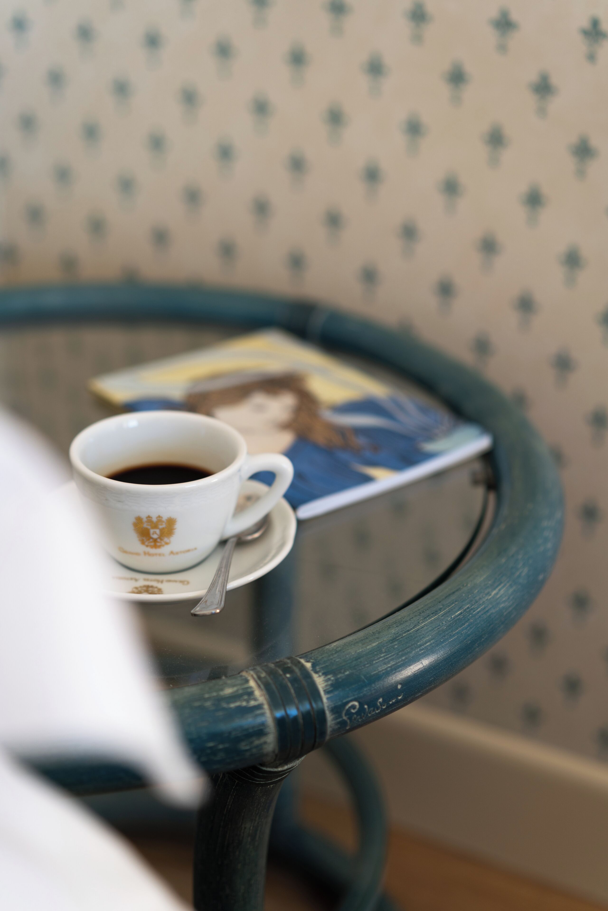 Uma chávena de café sobre uma pequena mesa, com um livro e uma colher.