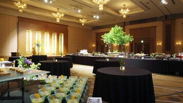 Un salón de banquetes con mesas redondas, una barra de bufé e iluminación decorativa.