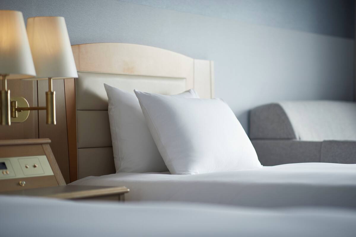 A neatly made bed with white linens and pillows, a wooden headboard, and a bedside table with lamps.