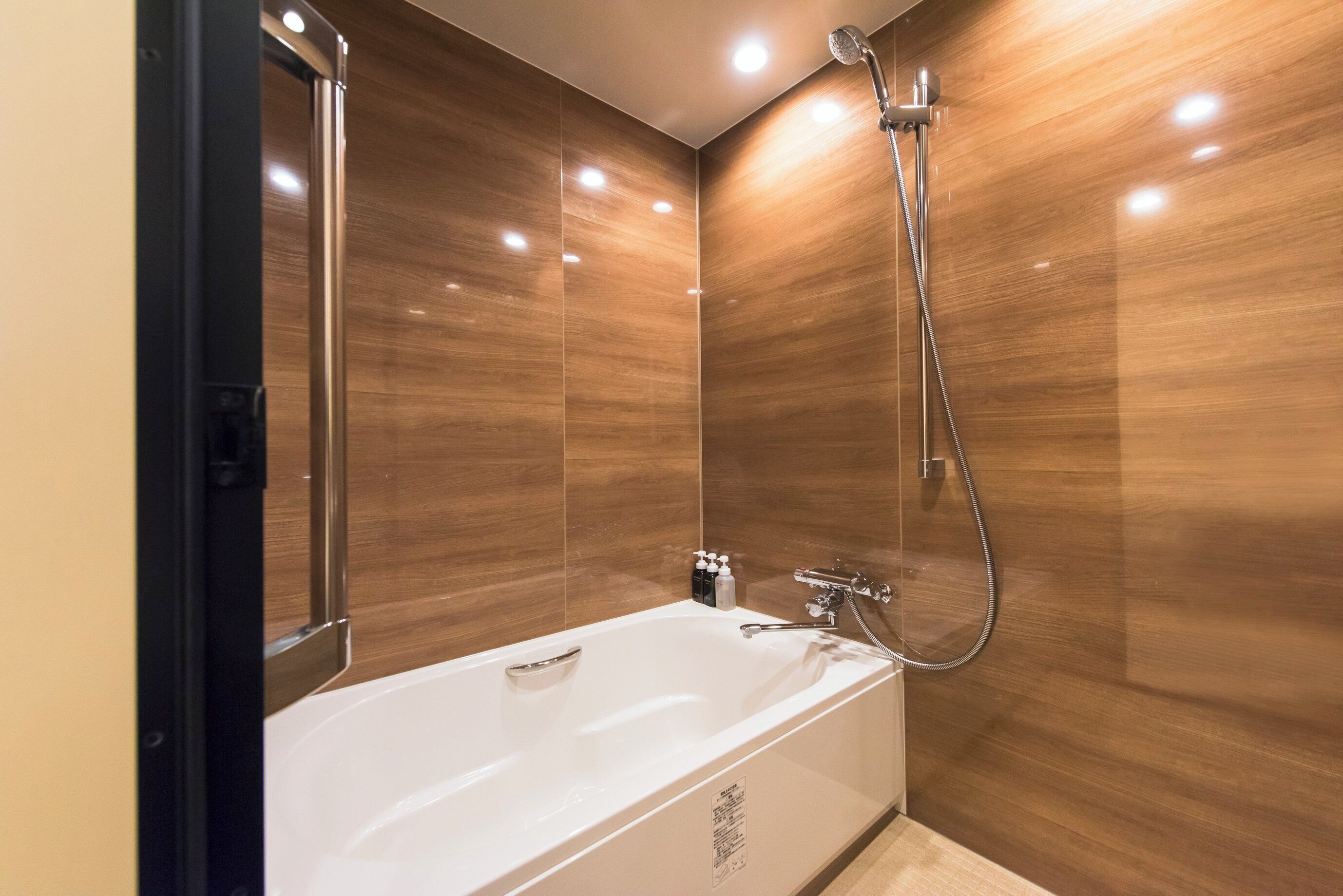 A modern bathroom with a white bathtub, a handheld showerhead, and a wall-mounted faucet.