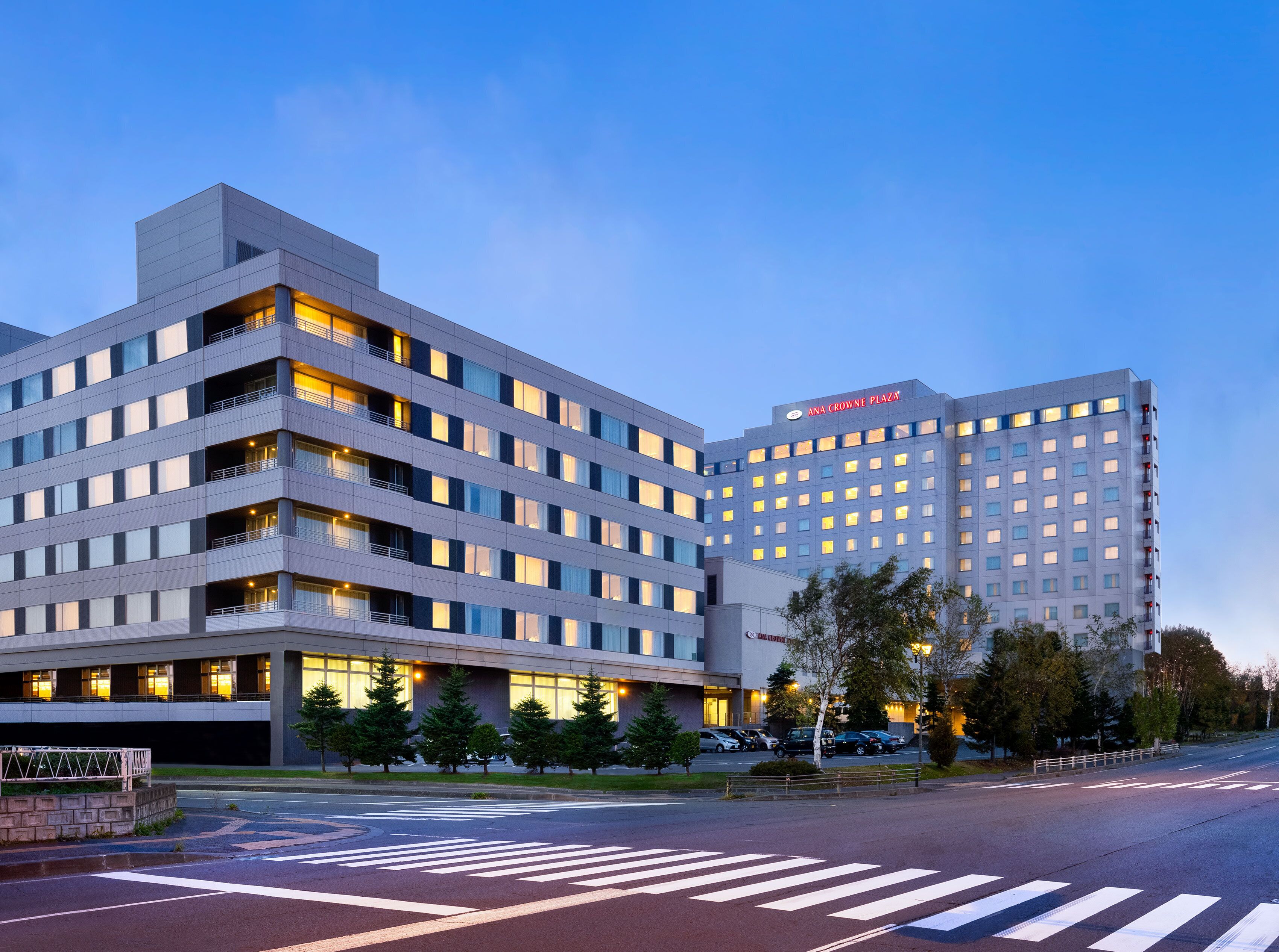 A multi-story hotel with a modern design, featuring a prominent sign for 'ANA CROWNE PLAZA' and a well-lit facade.