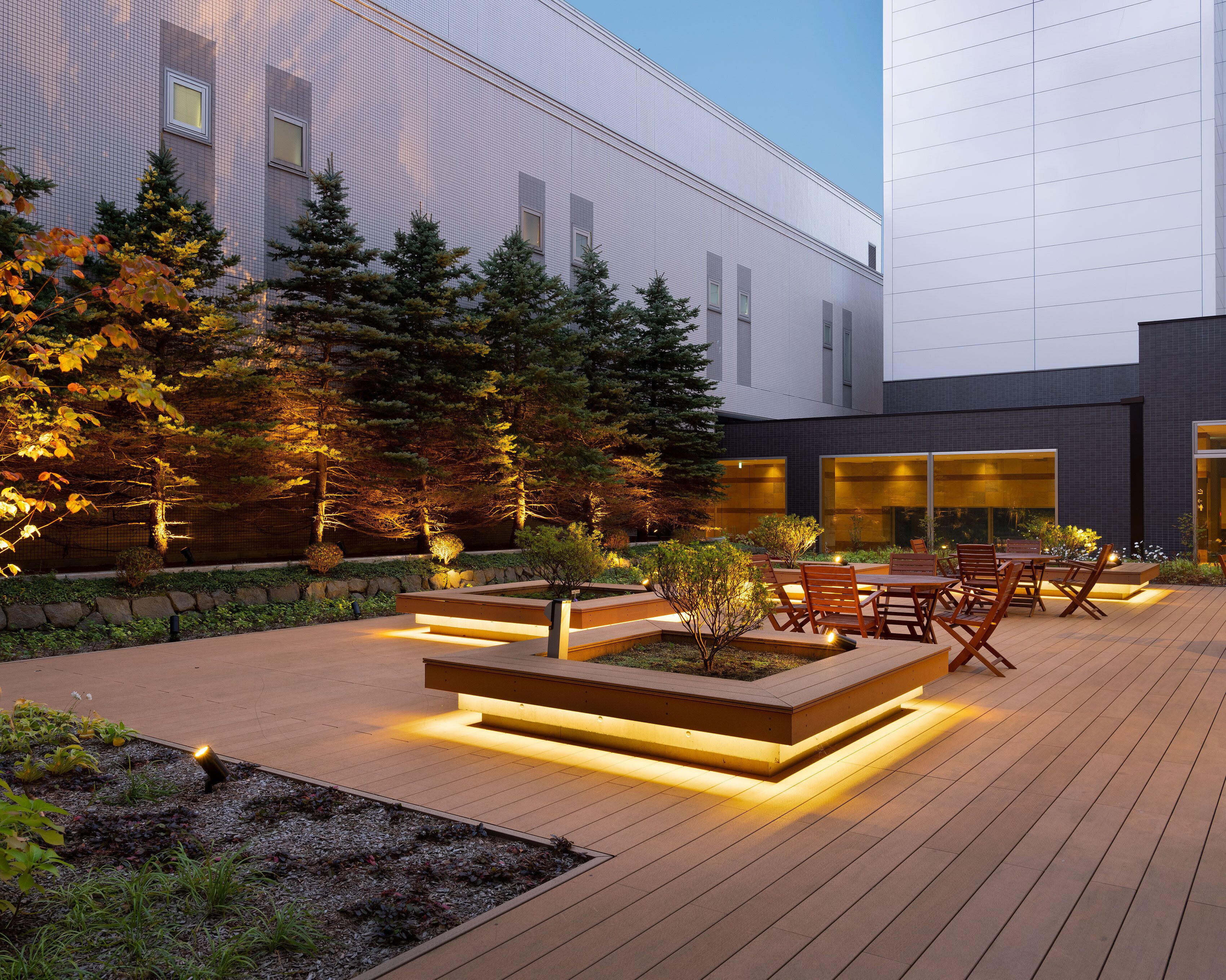Une terrasse extérieure moderne, dotée d’un revêtement de sol en bois, d’un espace aménagé avec des sièges et d’un jardin agrémenté d’arbres et de plantes.