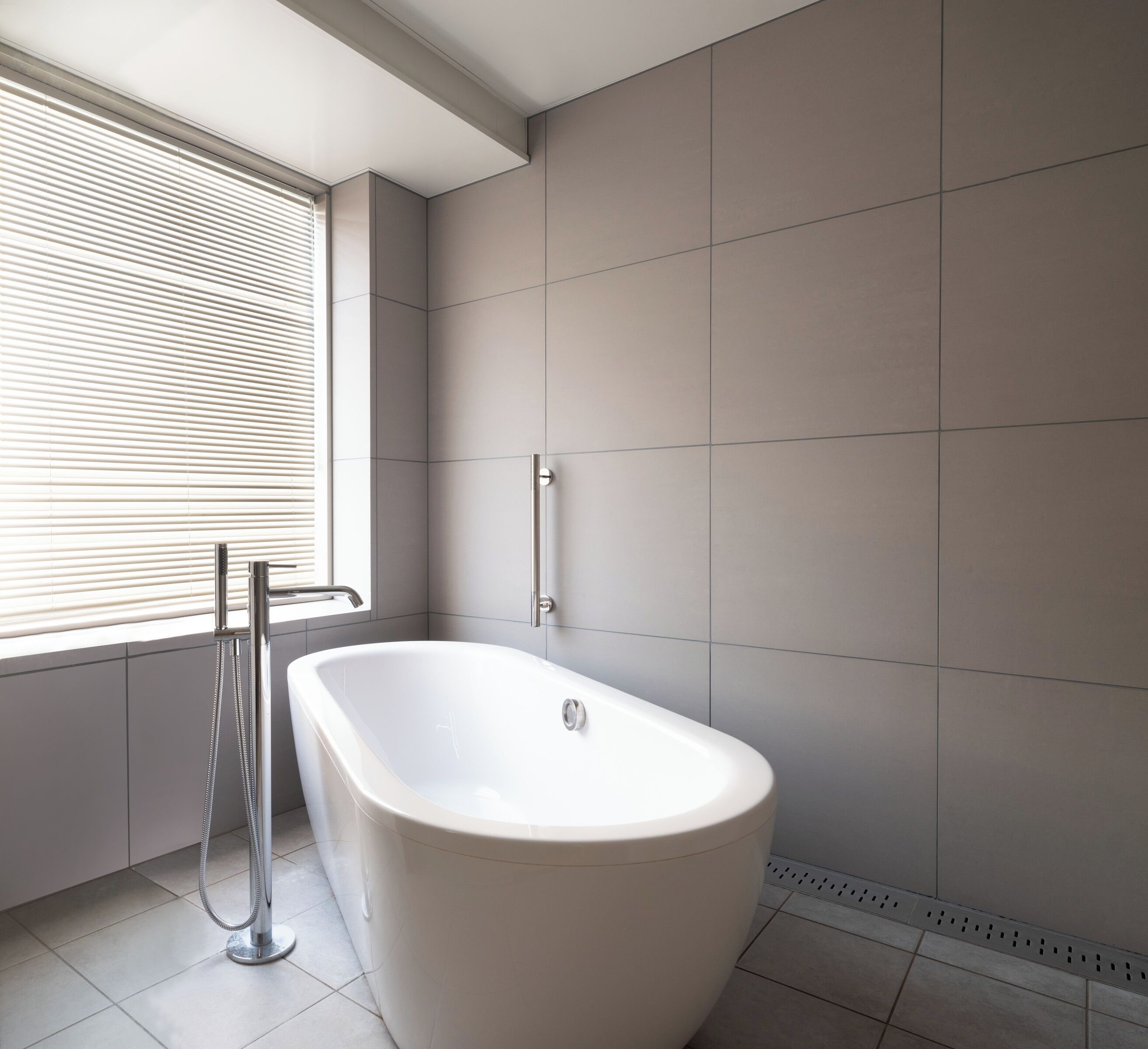 A modern bathroom with a freestanding bathtub, a window with blinds, and a towel rack.
