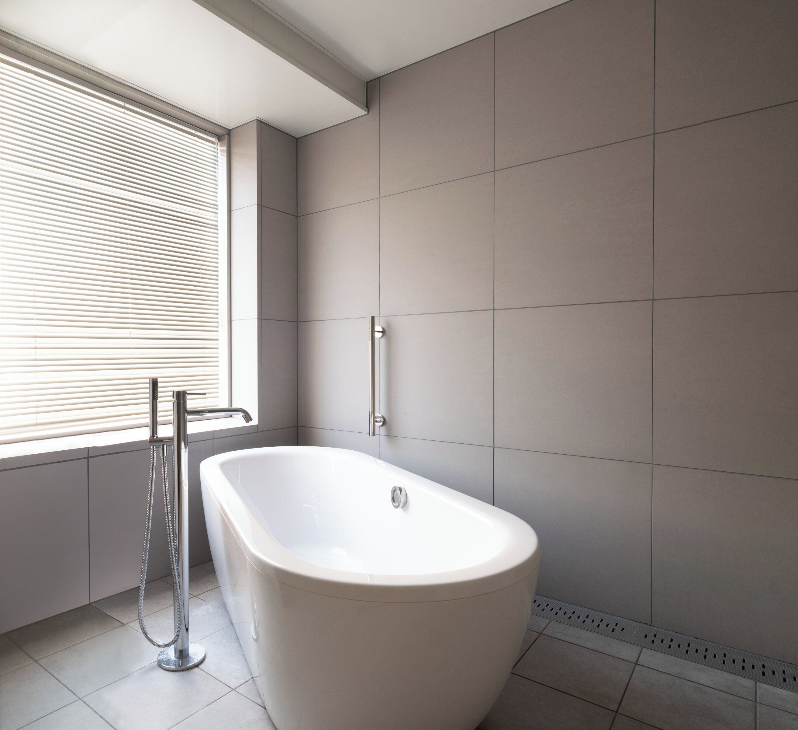 Un baño moderno con una bañera independiente, una ventana con persianas y un perchero para toallas.