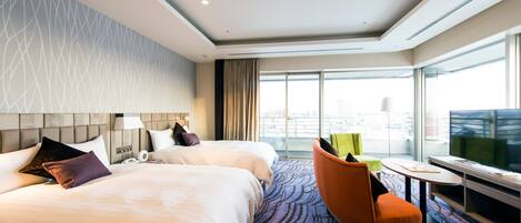 A hotel room with two beds, a desk, a chair, and a large window offering a city view.