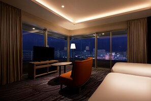 A hotel room with a large bed, a TV, a small table, and a chair. There is a view of the city at night through large windows. - ANA Crowne Plaza Chitose by IHG (Chitose)