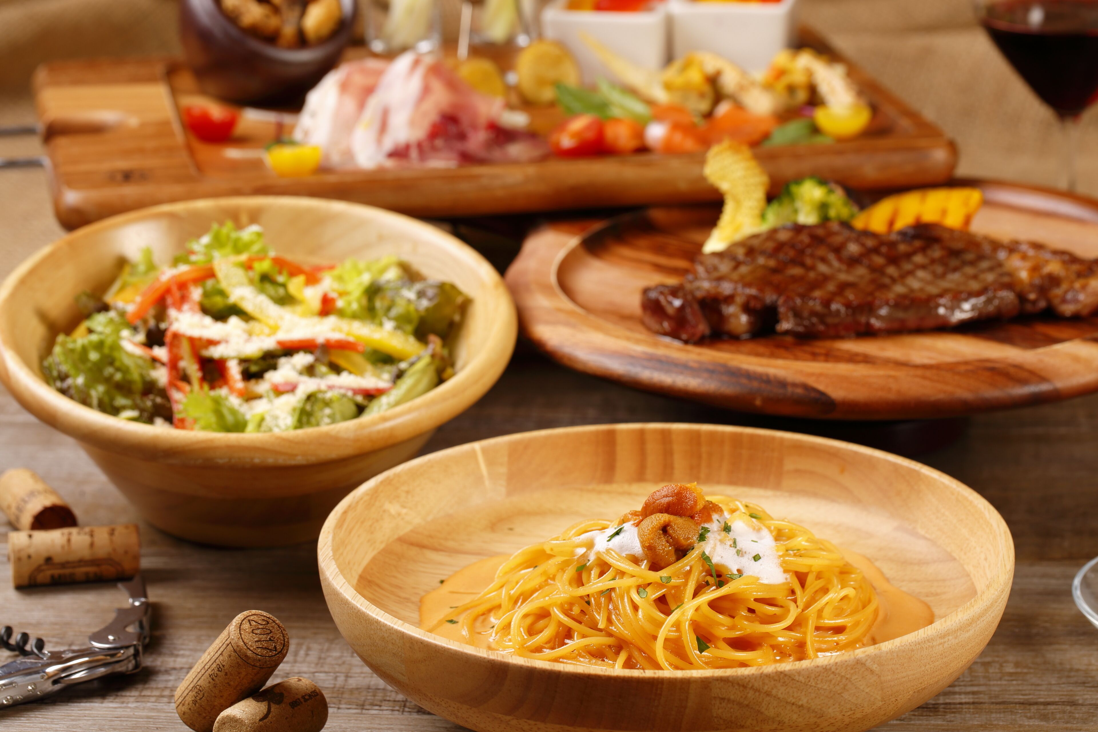 Una mesa de madera con tres platos de comida: pasta con salsa, una ensalada y un bistec.