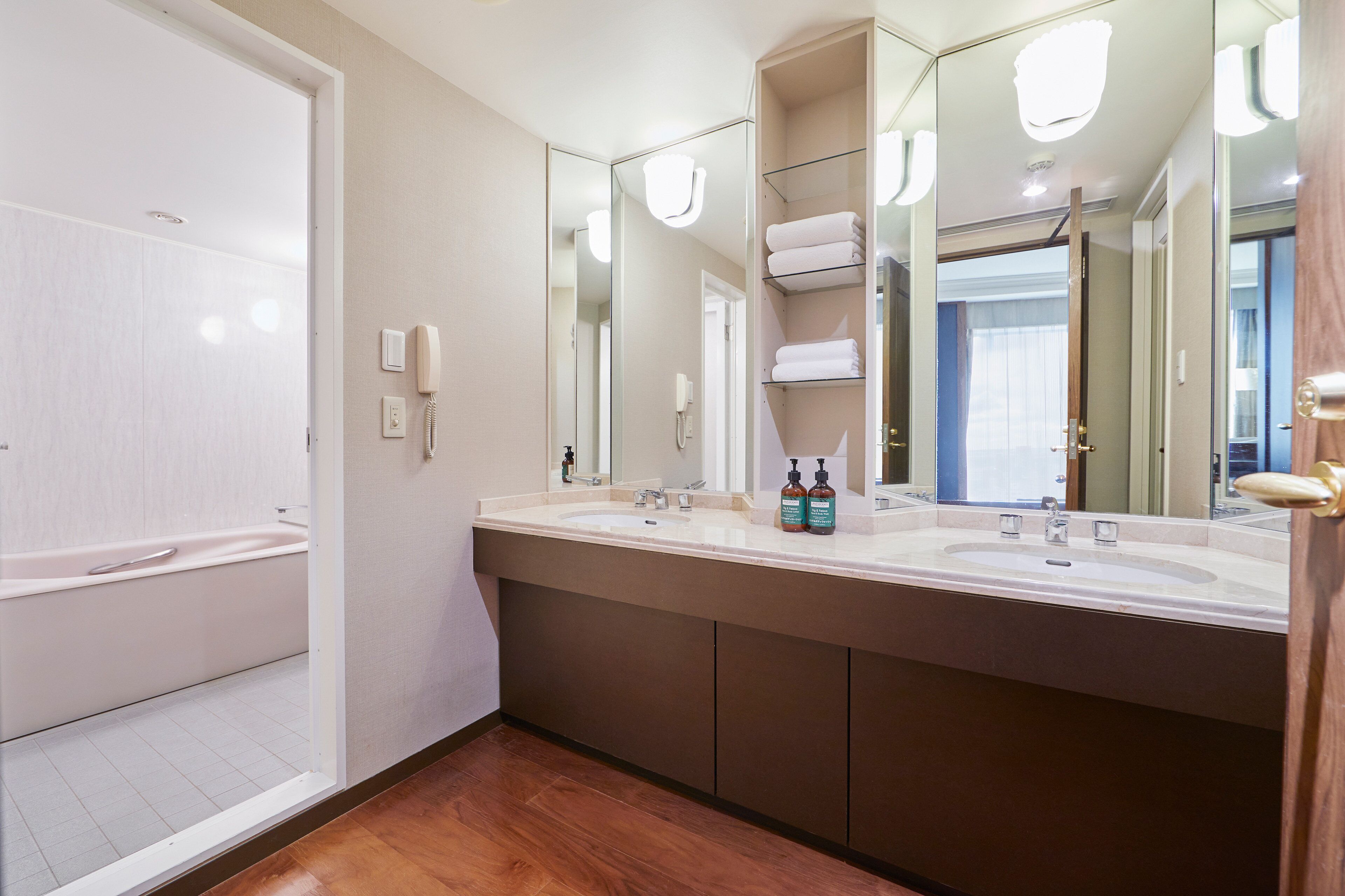 A modern bathroom with a double sink, a bathtub, and a large mirror.
