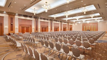 A large conference room with rows of chairs, ceiling lights, and a carpeted floor.