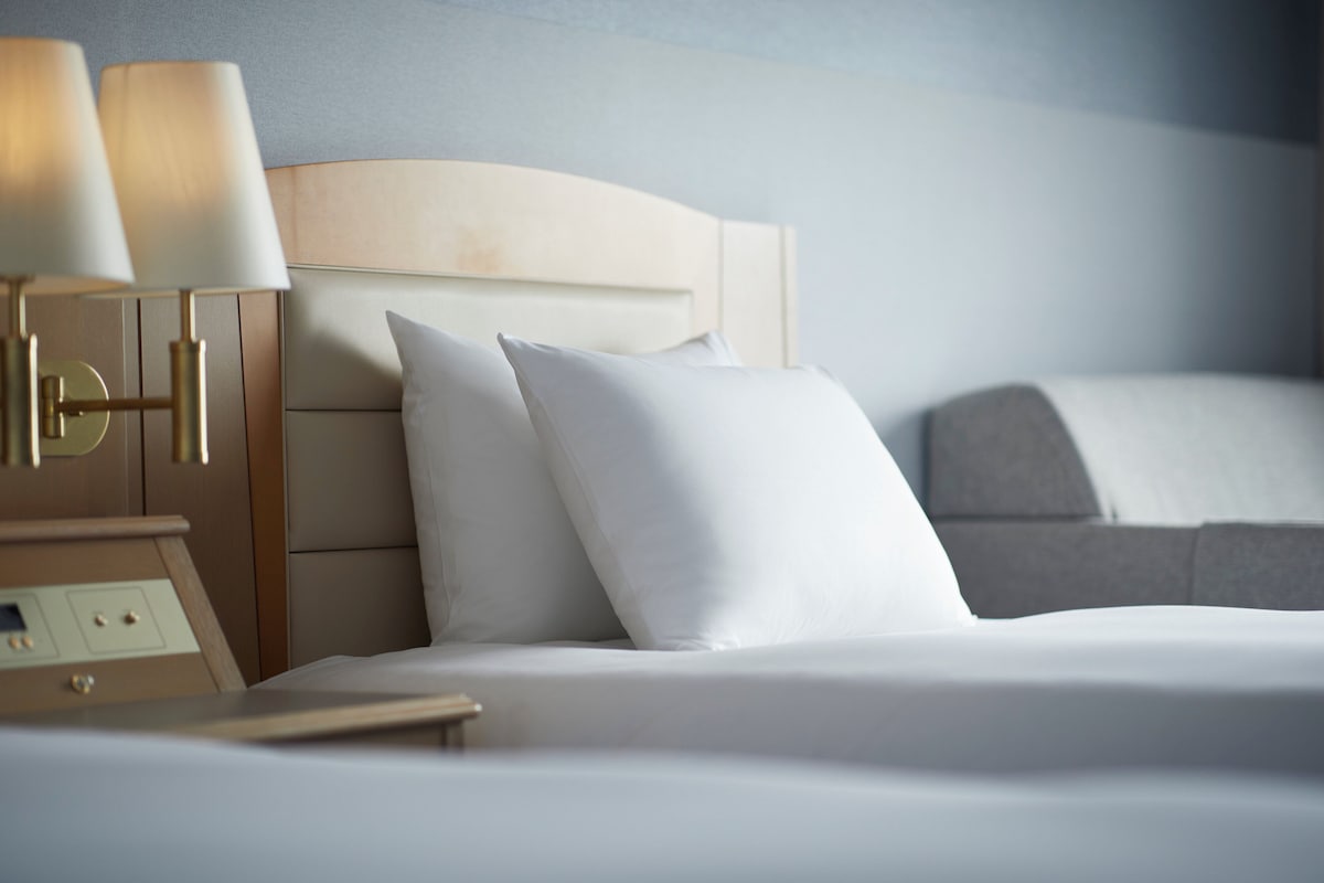 Una cama bien hecha con sábanas y almohadas blancas, cabecera de madera y mesita de noche con lámparas.