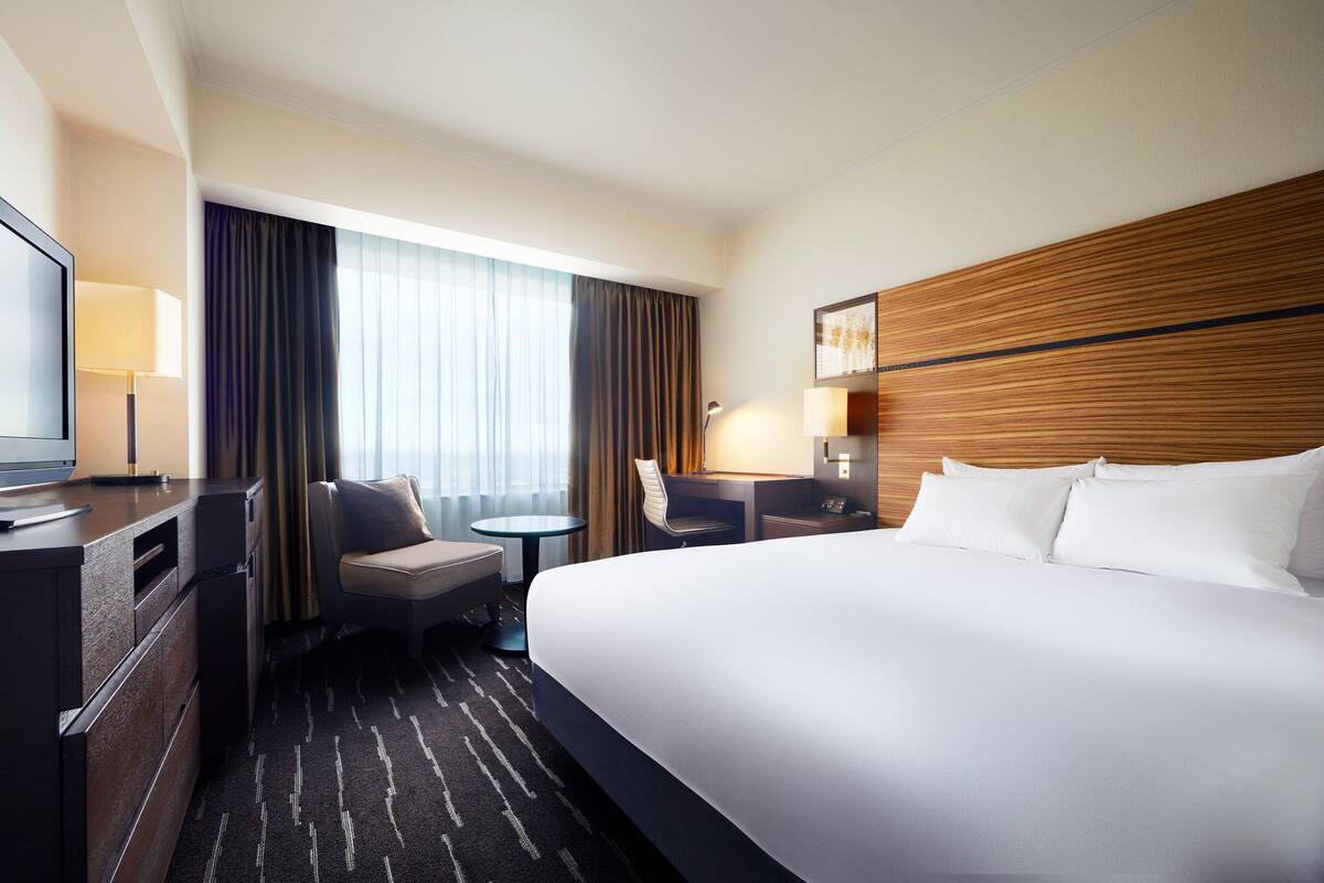 A hotel room with a large bed, a desk, a chair, a TV, and a window with curtains.