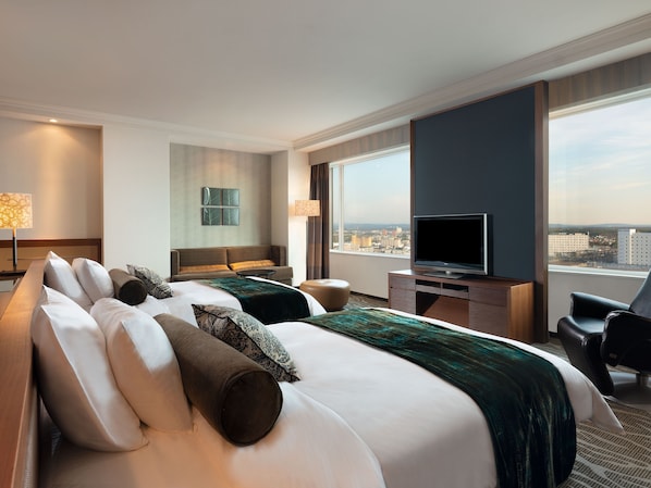 A hotel room with a large bed, a desk with a TV, a chair, and a view of the city.