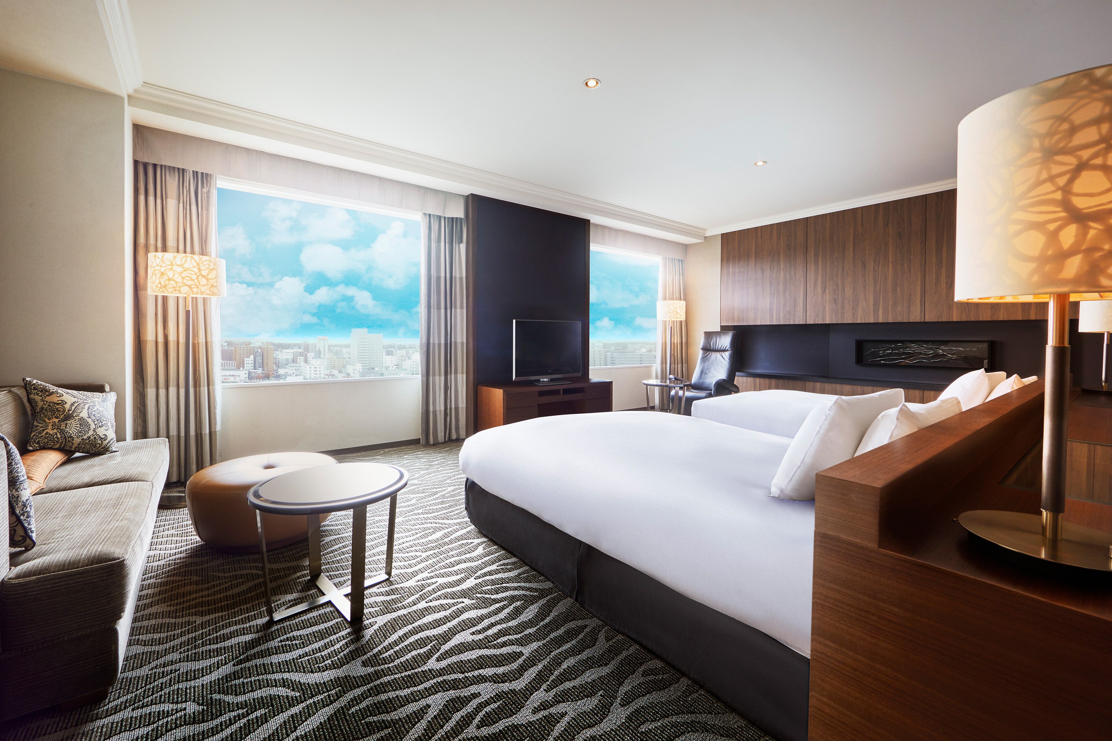 A modern hotel room with a large bed, a sofa, a small table, and a TV.