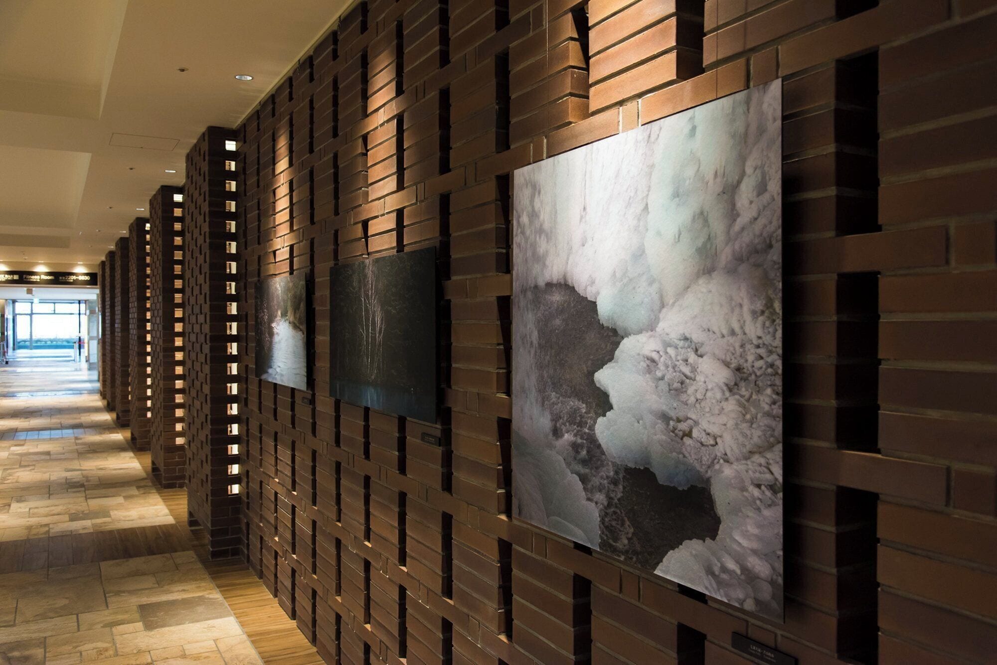 A corridor with a brick wall and framed artwork.