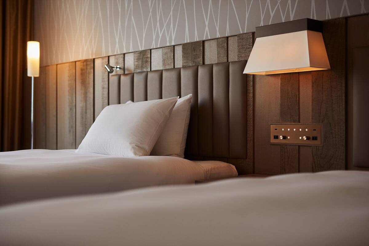 A hotel room with a wooden headboard, a bedside lamp, and a power outlet on the wall.