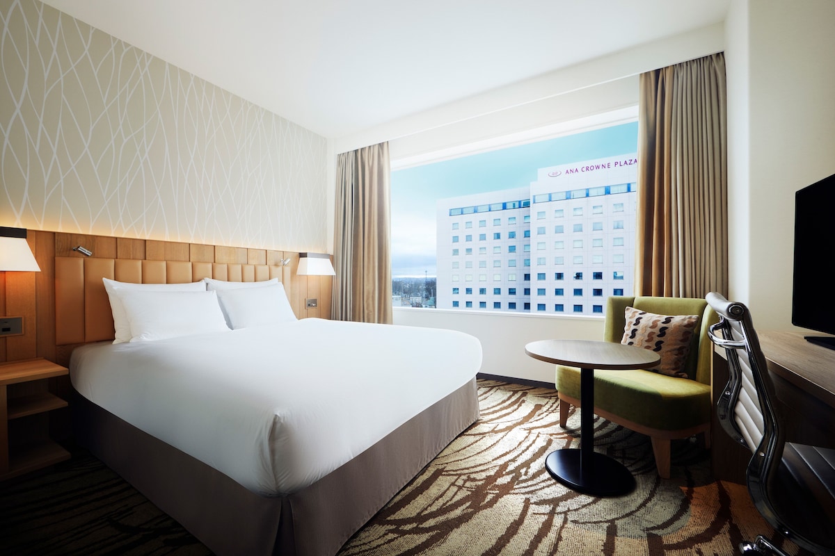 Habitación de hotel con una cama grande, un escritorio, una silla y vistas a un edificio.