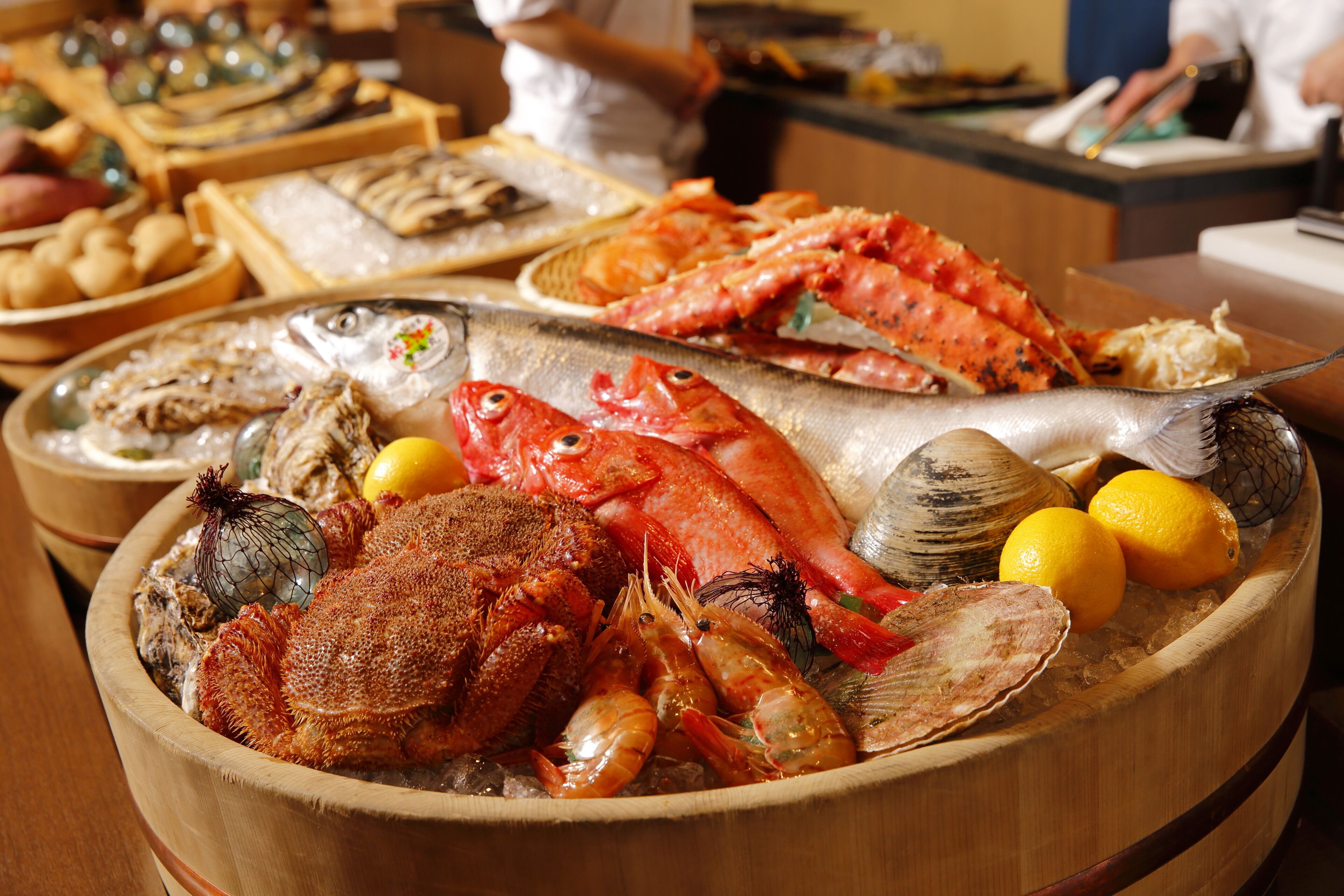 A wooden bowl filled with various seafood including lobsters, shrimp, and fish, with lemons and onions.