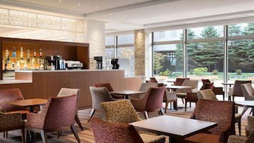 Un área de bar moderna con una variedad de botellas de licores, una máquina de café y un espacio de estar con sillas y mesas estampadas.