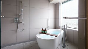 A modern bathroom with a freestanding bathtub, a showerhead, and a window providing natural light.