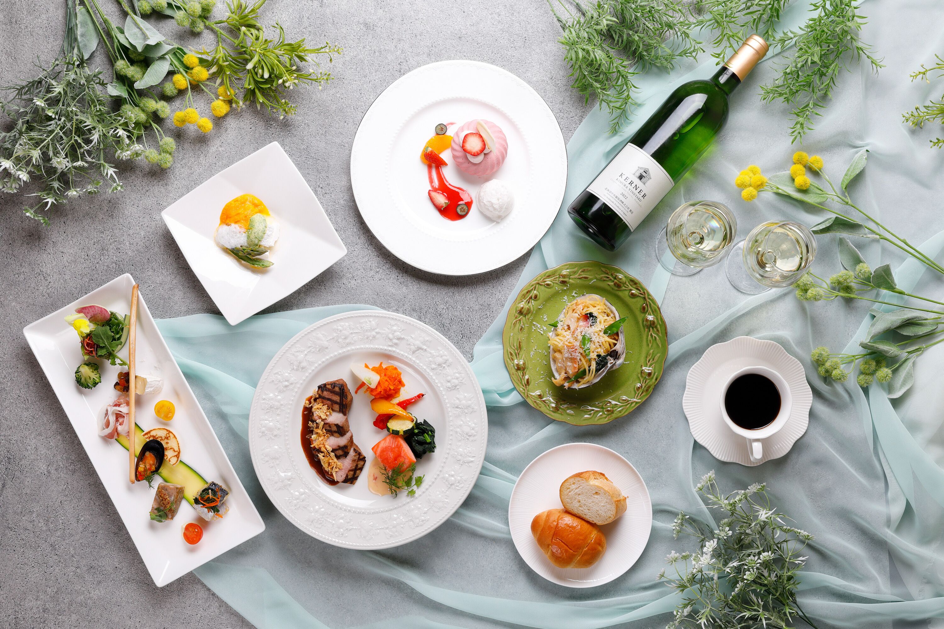 A variety of dishes and drinks on a table, surrounded by fresh herbs and flowers.