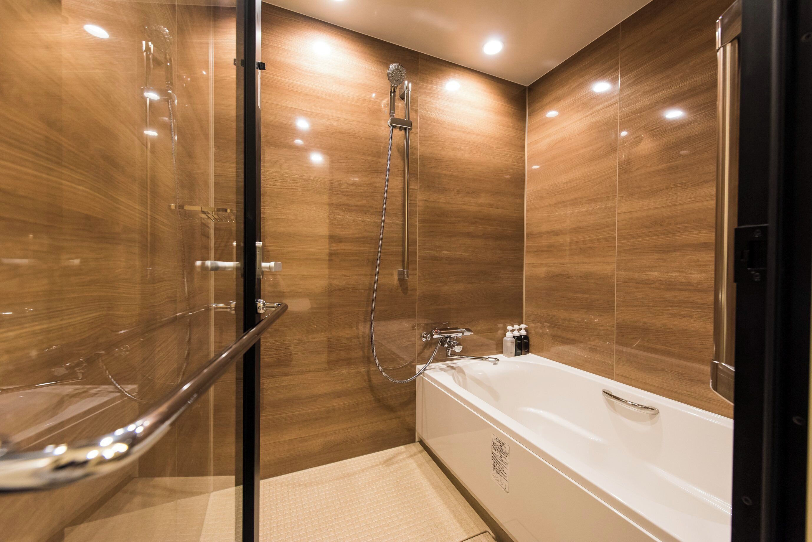 A modern bathroom with a glass shower enclosure, a white bathtub, and wooden paneling.
