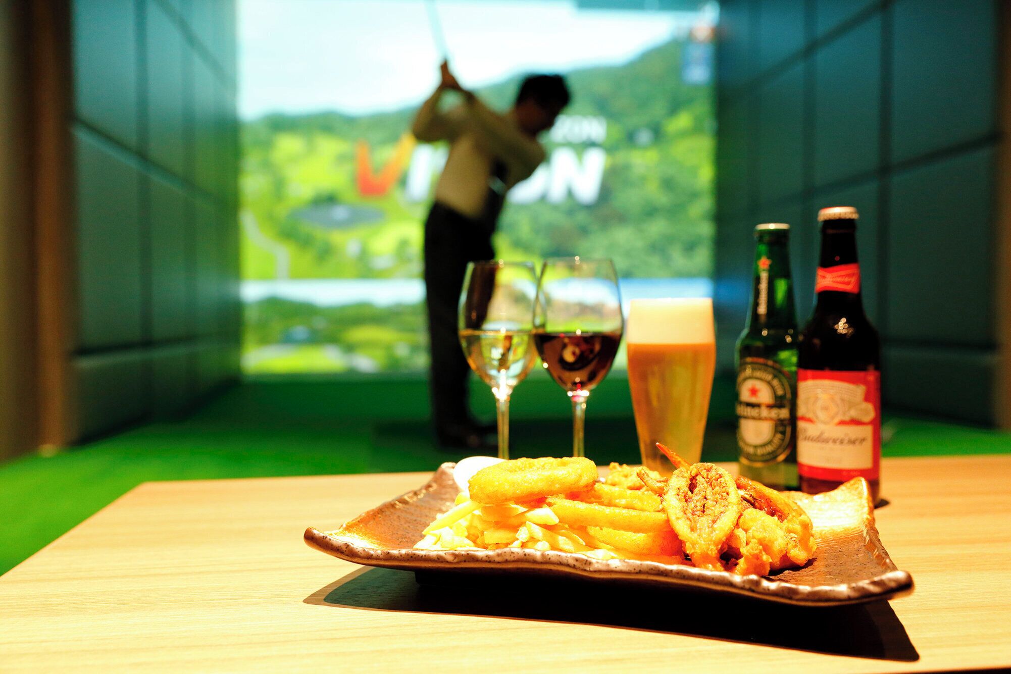 A table with a plate of food, two wine glasses, and two bottles of beer.
