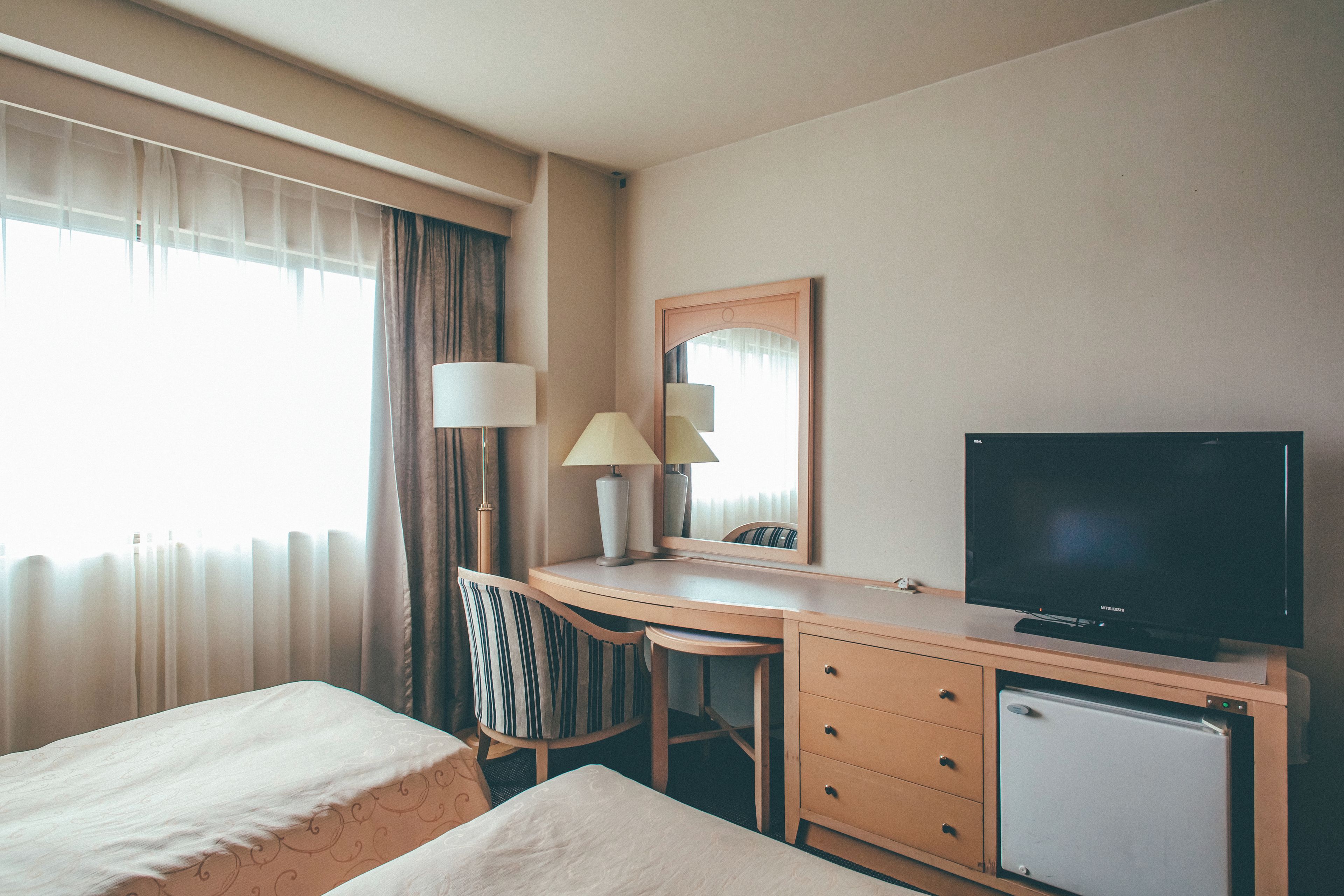 Habitación de hotel con cama, escritorio con lámpara, televisión y refrigerador pequeño.