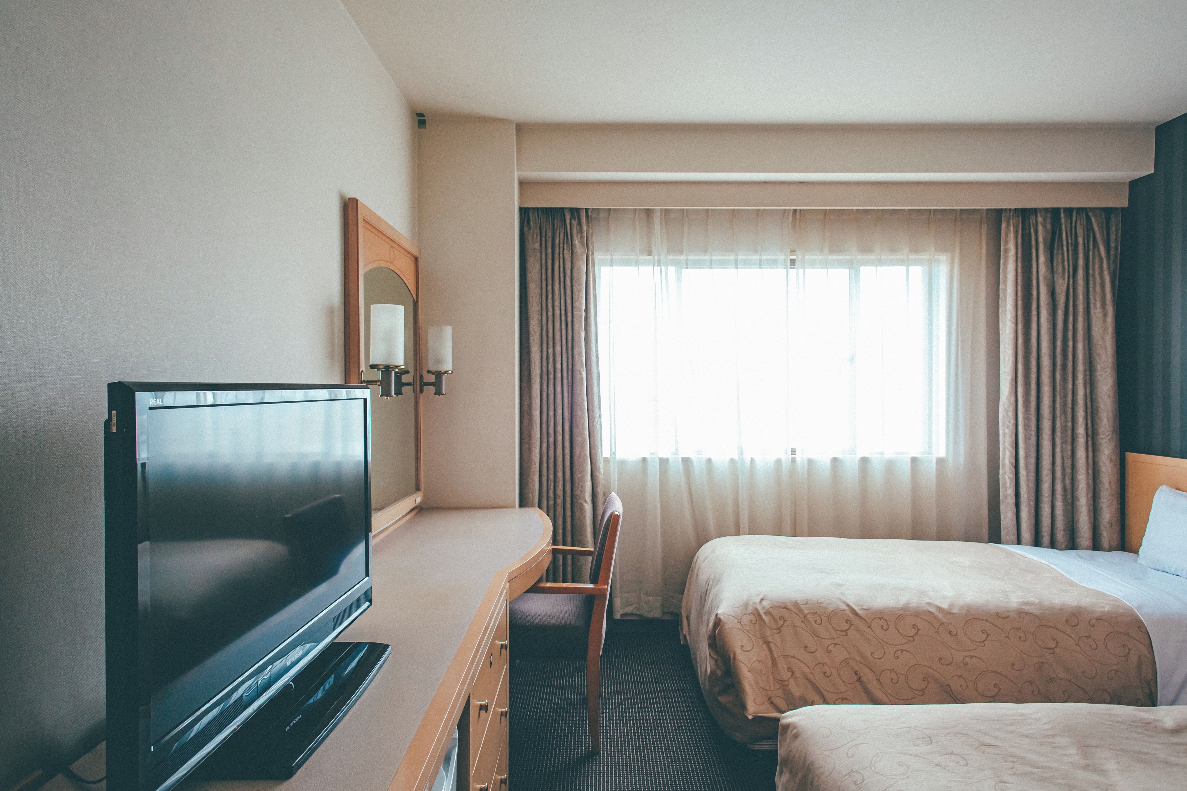 A hotel room with a flat-screen TV, a bed, a chair, and a window with curtains.