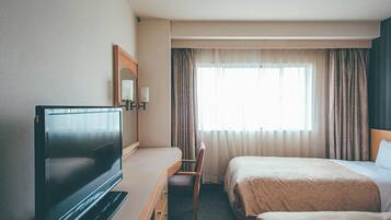 A hotel room with a flat-screen TV, a bed, a chair, and a window with curtains.