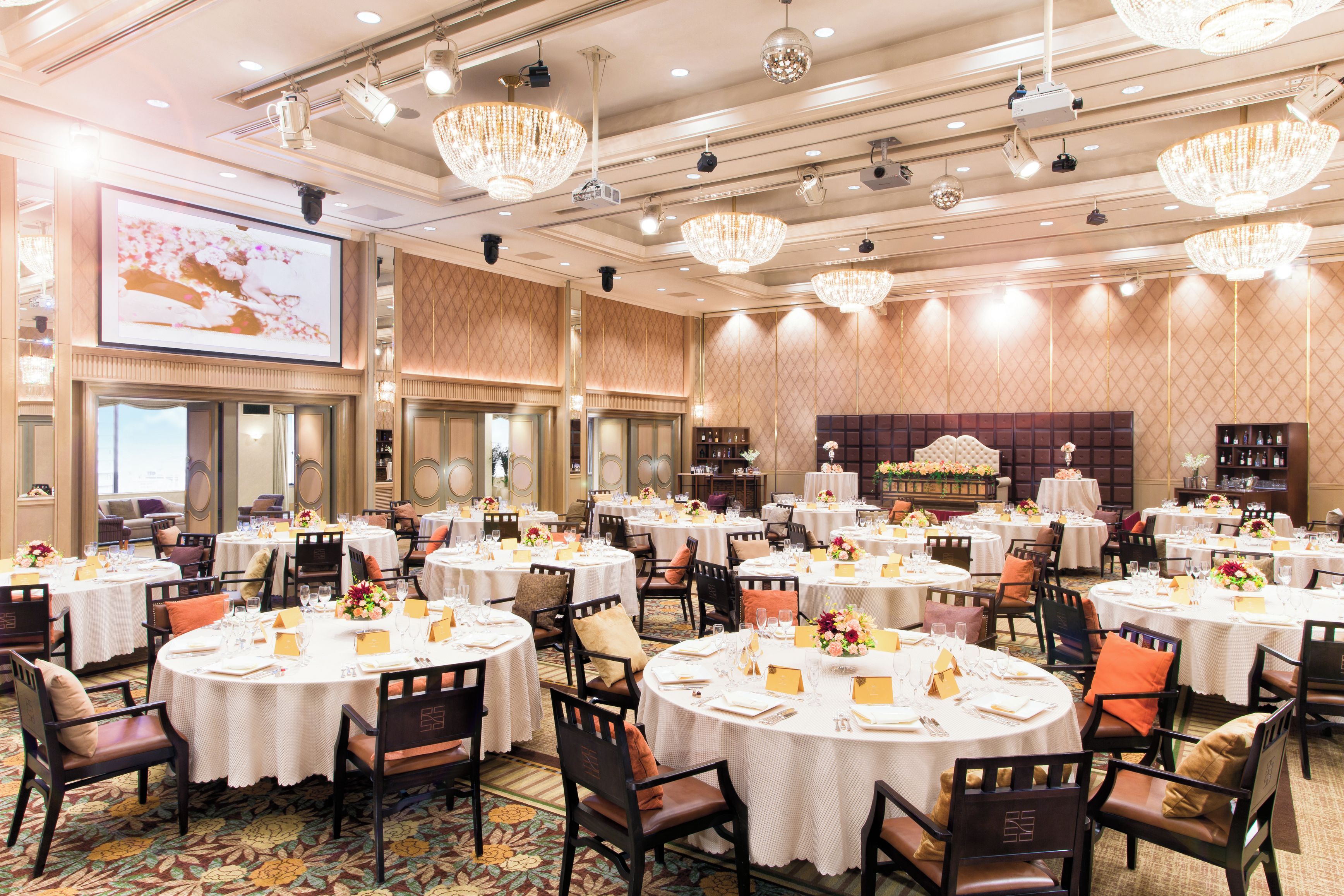 A banquet hall with round tables, chairs, and chandeliers.